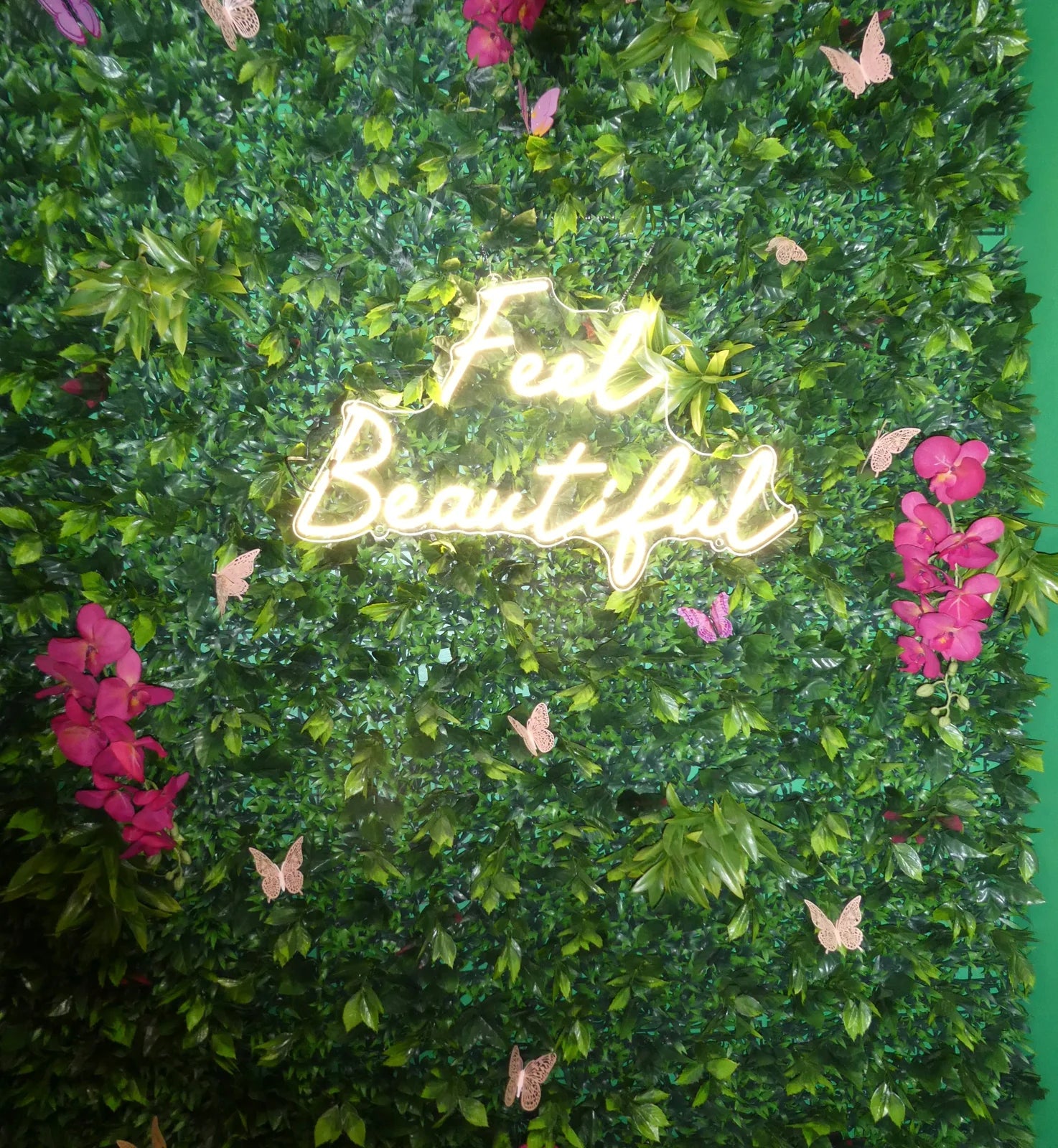 Feel Beautiful neon sign on a leafy wall with pink butterflies